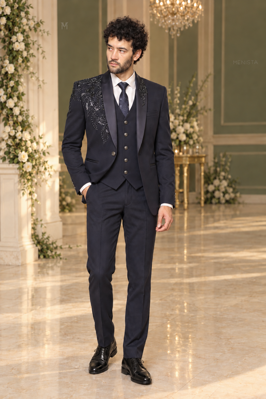 Michael wearing Menista Cassian navy floral beaded three-piece tuxedo with satin shawl lapels, full front view in a cream and sage wedding hall.