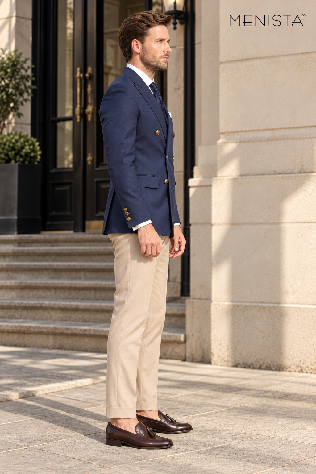 Side profile of Menista navy blazer and beige trousers showing the tailored silhouette and three brass cuff buttons.