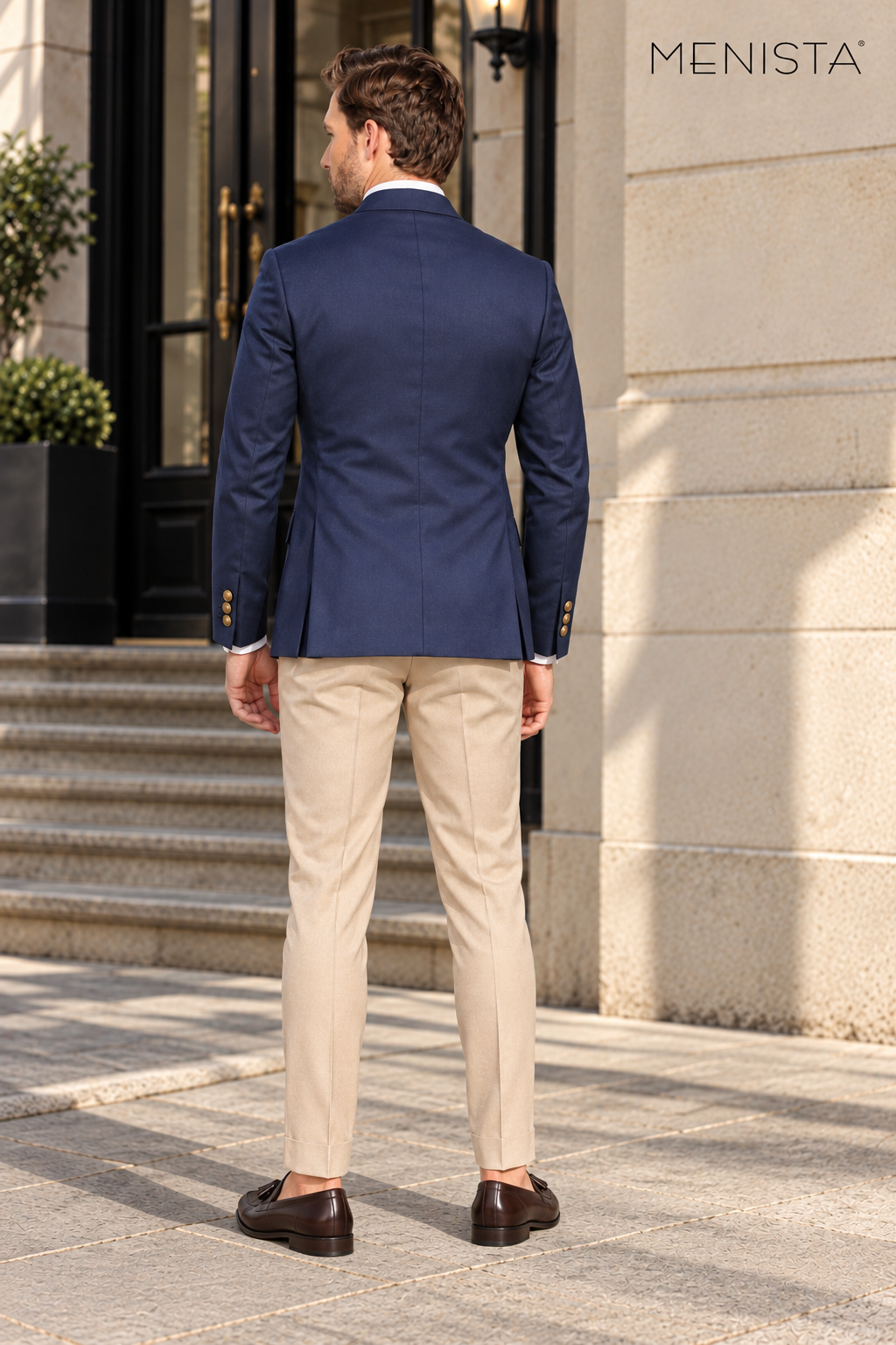 Back view of Menista navy jacket with plain centre seam and twin side vents, worn with beige trousers.
