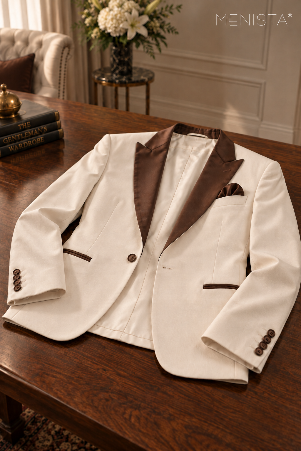 Menista ivory jacket resting flat on a wooden table, showing brown satin peak lapels, one front button, one buttonhole and four cuff buttons per sleeve.