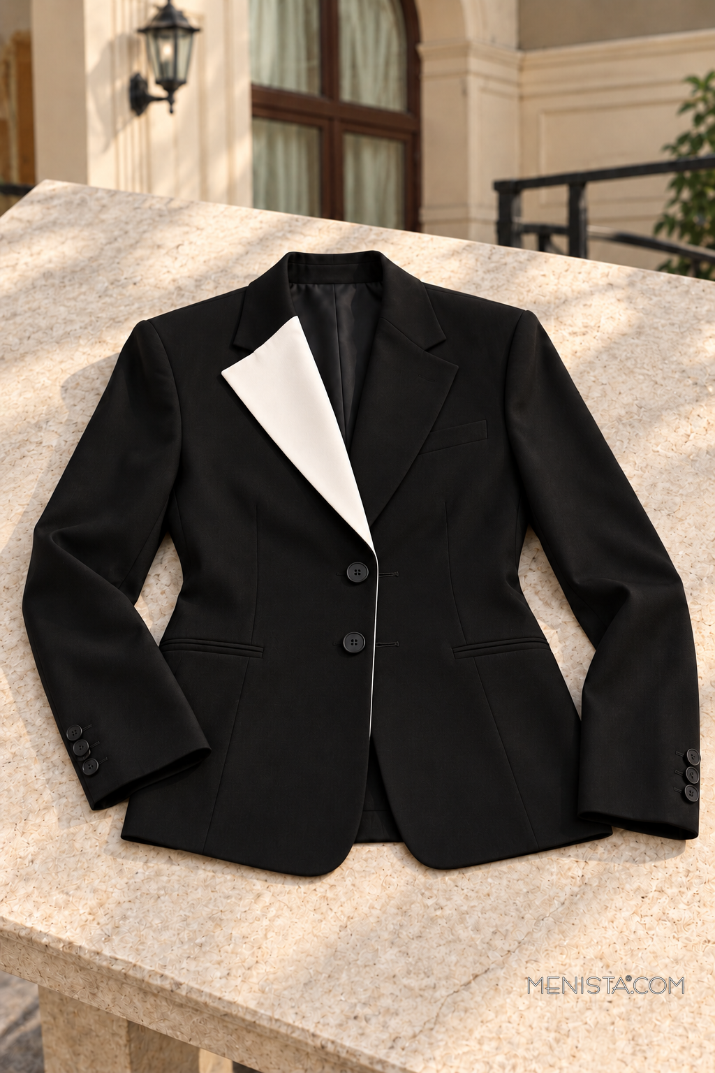 Caldric black and ivory two-button jacket on a pale stone table, showing buttons and buttonholes.